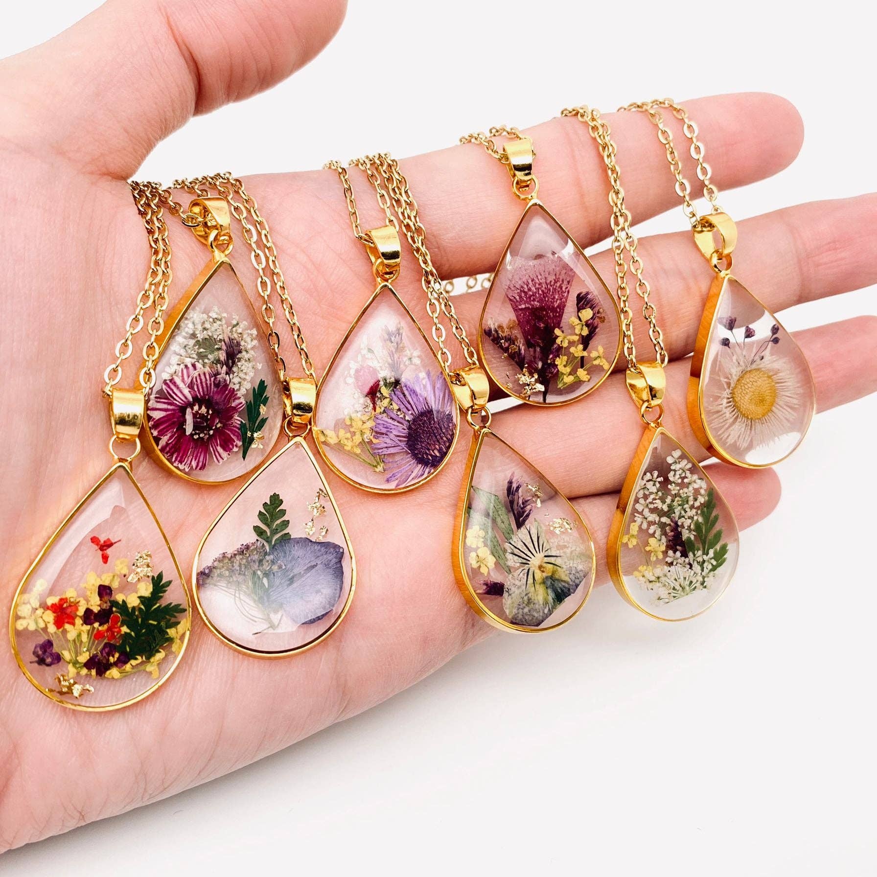 Pressed flower charm necklaces draped over a hand